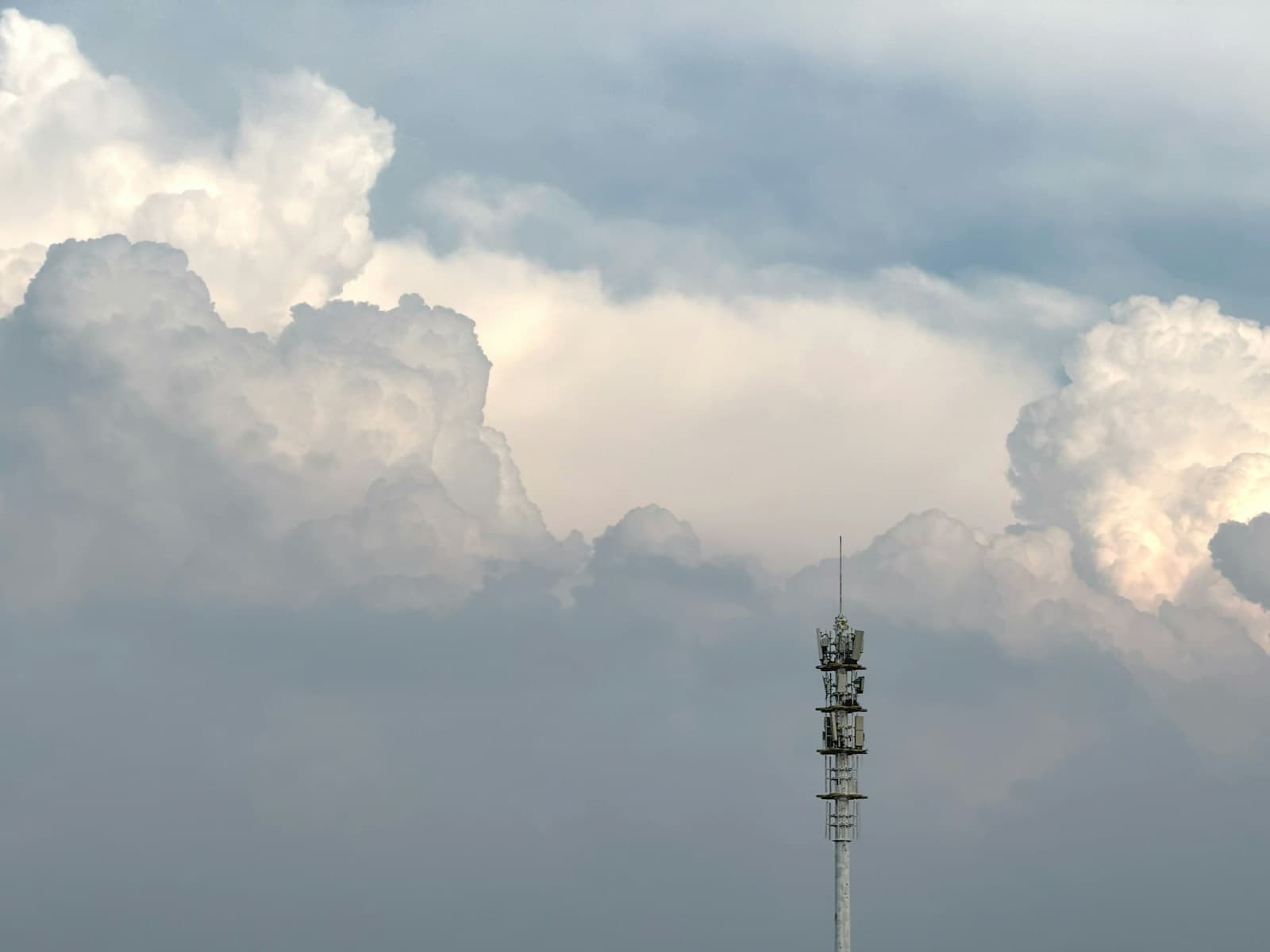 A slender communications mast against a bank of cloud
